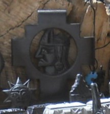 Schwarze Figuren,
                    Nahaufnahmen des Mutter-Erde-Kreuz mit einem
                    Inkakopf drin und Sonne mit Gesicht daneben